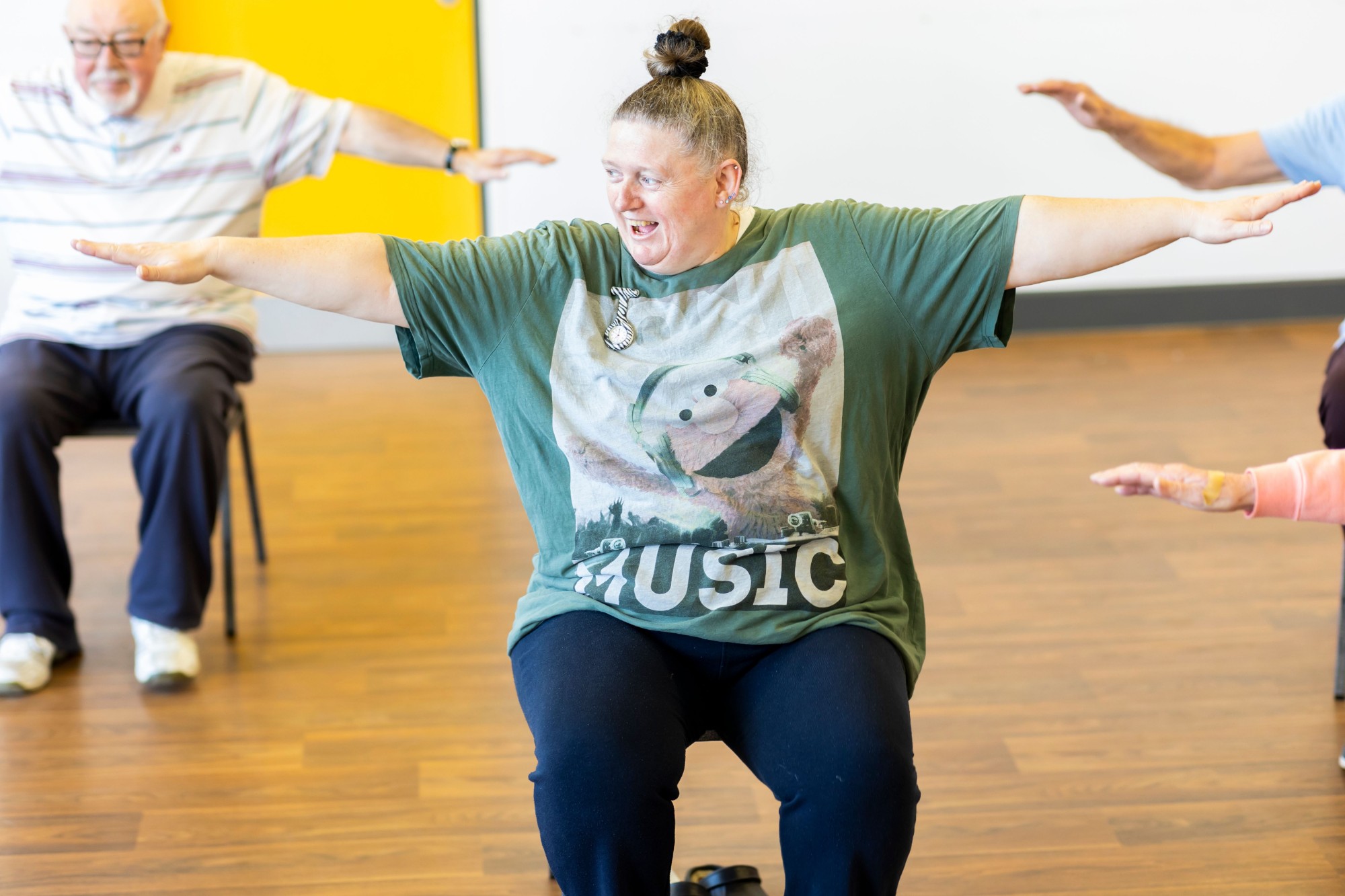 Instructor leading a seated exercise class with arms outstretched