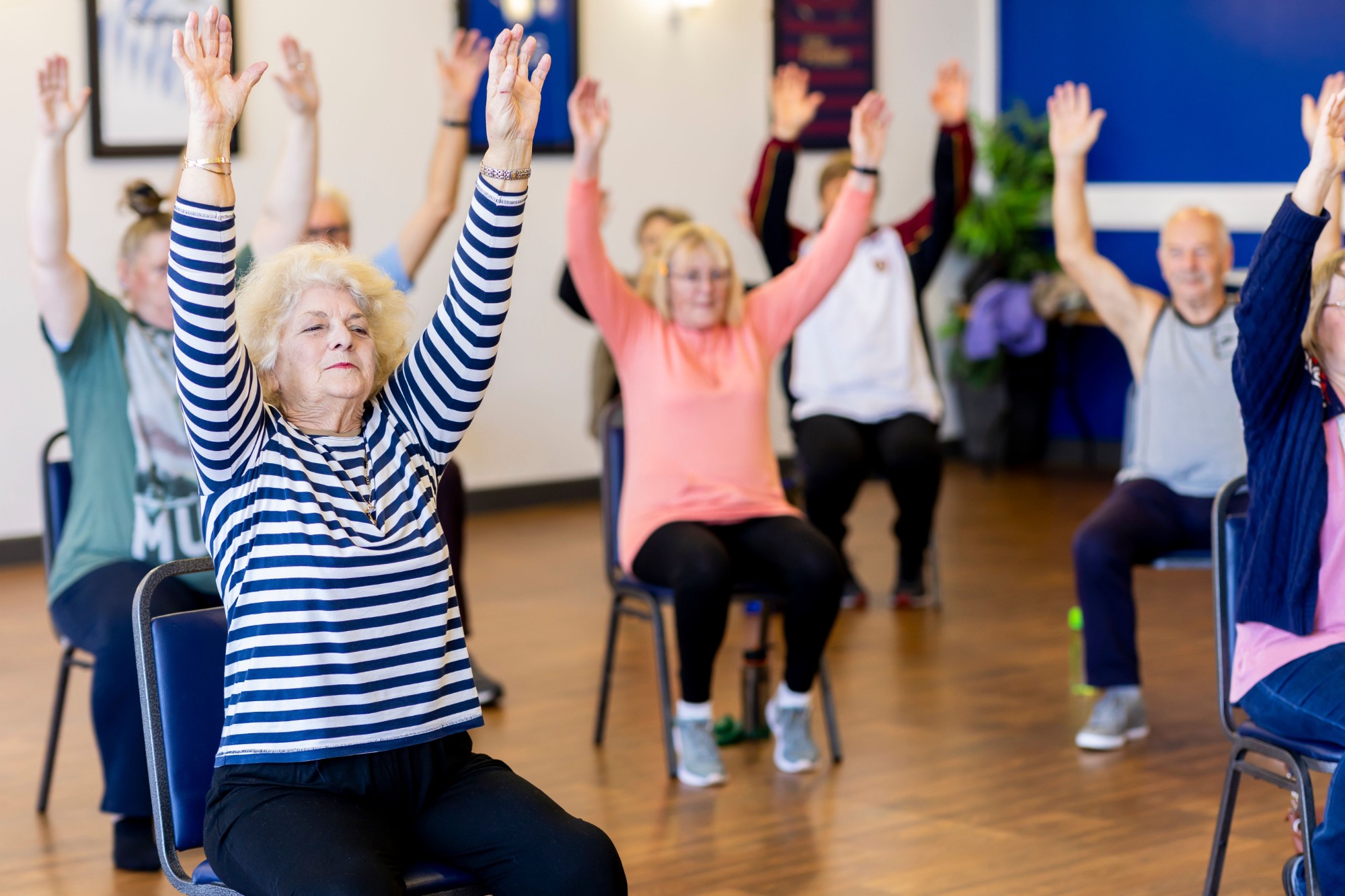 Group of seniors raising their arms in a seated exercise class